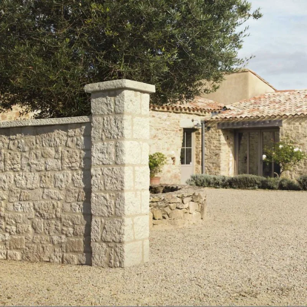 un pilier bridoire collé à un muret devant une maison en pierre